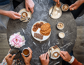 Bovenaanzicht tafel met koffie en assortiment Jules Destrooper koekjes op bord.